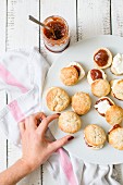 A woman's hand reaching for scones with jam and clotted cream
