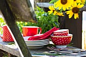 Red and white picnic crockery and cutlery on rustic wooden bench next to sunflowers