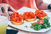 Frauenhand greift nach Bruschetta mit Tomaten