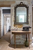 Typewriter and candelabra on antique console table below mirror on wall