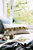 Cozy seat by the window with pillows, magazine and cup