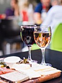 Rotwein- und Weissweinglas neben Käsebrett mit Schinken in einem Restaurant in Bordeaux, Frankreich