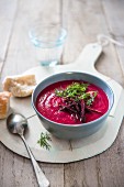 A bowl of beetroot soup with a dill garnish and bread