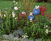Clay bird in a bed with roses, Penstemon, Helichrysum