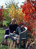 Junge Frau auf Bank am Herbstbeet