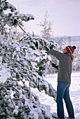 Junge Frau schüttelt Schneelast mit Besen
