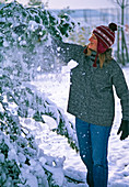 Junge Frau schüttelt Schnee von den Zweigen
