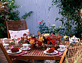 Tischdeko mit Gesteck von Rosenblüten, Rosa (Hagebutten), Viburnum (Schneeballbeeren)