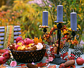 Metallkorb mit Malus (Äpfel und Herbstlaub), Kerzenhalter mit blauen Kerzen