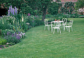 Frühsommerliches Staudenbeet mit Delphinium (Rittersporn), Digitalis (Fingerhut), Iris (Schwertlilien), Salvia (Salbei), weiße Sitzgruppe auf dem Rasen