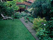 Small city garden with Alchemilla (lady's mantle), Spiraea japonica 'Golden Princess' (Japanese pine), wooden lounger next to Robinia (black locust) - on the lawn