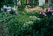 Terrassenbeet an ländlicher Terrasse mit weißer Sitzgruppe, Hosta (Funkien), Astilbe (Prachtspiere), Rosa (Rosen), Salvia nemorosa (Steppensalbei, Ziersalbei), Stachys (Ziest), Geranium (Storchschnabel)