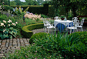 White seating area on a round terrace, Buxus (boxwood) hedge and balls, lush perennial bed with Hosta (hosta), Astilbe (daisy), Geranium (cranesbill) and Rosa (roses)