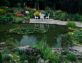 Seating area on paved terrace by the pond, Nymphaea (water lilies), colourful perennial bed with Coreopsis (girl's eye), Astilbe (daisy)