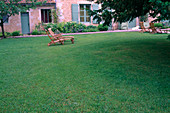 Rasen, Liegestühle aus Holz, Haus im Hintergrund