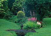 Kleiner Bach im Garten mit Steg aus Brettern, Beet mit Astilbe (Prachtspieren), Koniferen und Farn
