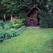 Gartenhaus mit Backofen und blauer Sitzgruppe, im Beet Alchemilla (Frauenmantel), Digitalis (Fingerhut), Centaurea (Flockenblume)