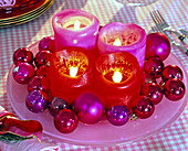Moderner Adventskranz mit pinkfarbenen und roten Kerzen auf rosa Glasteller
