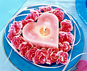 Blüten von Dianthus (Nelken, rosa), um rosa Kerze in Herzform gelegt