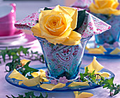 Flower of Rosa (rose, yellow) in small blue vase, patterned napkin