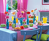 Frühstückstisch mit Dianthus (Nelken) in blauen Flaschen , Orangensaft