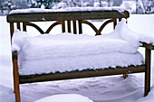 Thickly snow-covered wooden bench in the garden