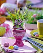 Ostergras in rosa Eierbecher ausgesät, Holzblüten, Zuckereier, Serviette