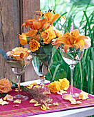 Lilium (Lilien, orange), Rosa (Rosen, orange) in Gläsern mit Fuß, Gräser