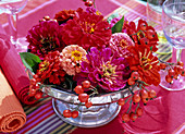Zinnia (zinnias) and rose hips in a silver bowl on a red tablecloth