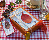Verpacktes Geschenk, darauf handgeschöpftes Papier, dekoriert mit Herbstlaub