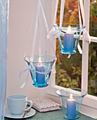 Gläser mit blauen Stumpenkerzen im Fenster hängend, Tasse, Buch
