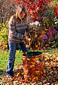 Junge Frau füllt Laub in Gartenabfallsack