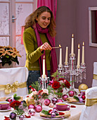 Woman lighting candles on the table, decorated with pinks (roses), abies (fir)