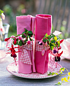 Fuchsia (Fuchsien) mit Bändern an zusammengerollten, rosafarbenen Servietten