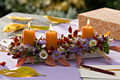 Herbstgesteck mit Kerzen, Astern und Hagebutten