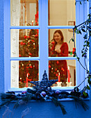 Blick von außen ins Weihnachtszimmer, Frau zündet Kerzen an