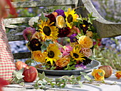 Wreath of sunflowers, roses and dahlias on a wine box leaning against a bench