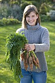 Young woman holding a bunch of carrots (Daucus)