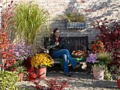 Frau auf herbstlicher Terrasse mit Stauden und Gräsern