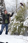 Mann schüttelt Schnee mit Besen von Sinarundinaria (Bambus)