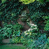 Water Feature: WALL MOUNTED CERAMIC SNAKE FOUNTAIN SURROUNDED by FOLIAGE. Designer: Lucy Smith