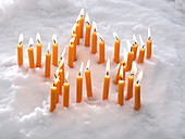 Burning yellow candles in star shape in the snow