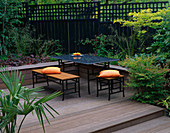 BELAU DECK TERRACE with Black MARBLE TABLE AND CHAIRS, Orange CUSHIONS, Black FENCE AND TRELLIS, ROBINIA AND NANDINA DOMESTICA. Designer: Sarah LAYTON