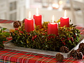 Adventskranz aus Ilex (Stechpalme) mit roten Kerzen auf Holzuntersetzer