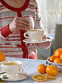 Frau mit heißem Orangentee in Tasse, Orangen