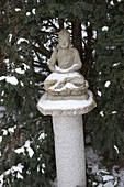 Verschneiter Buddha auf Granitsäule in Nische von Taxus (Eibe)