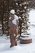 Snow-covered terracotta figurine in front of Carpinus hedge