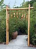 Bambustor als Eingang in asiatischen Garten mit Phyllostachys (Bambus), Windspiel aus Bambusrohren, brauner Kübel, Buddha-Figur
