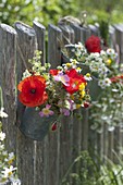 Small meadow bouquet in zinc cups hung on fence