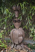 Frauenfigur aus Corten-Stahl vor Bambus-Hecke